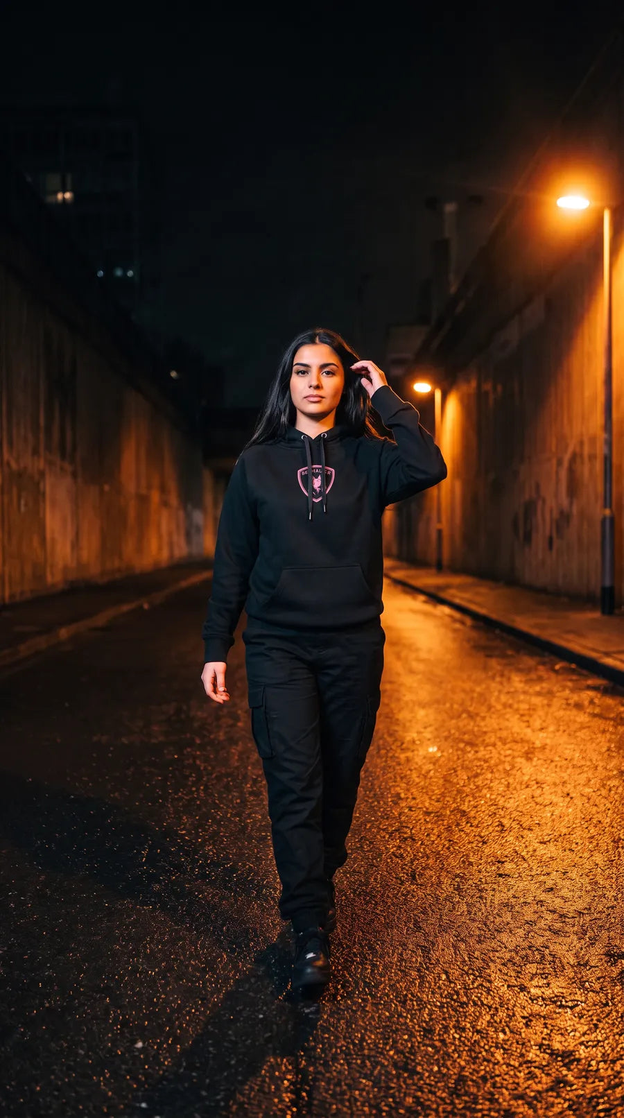 Frau im schwarzen Benhauser Hoodie mit rosa Wappen in einer Unterführung bei Nacht