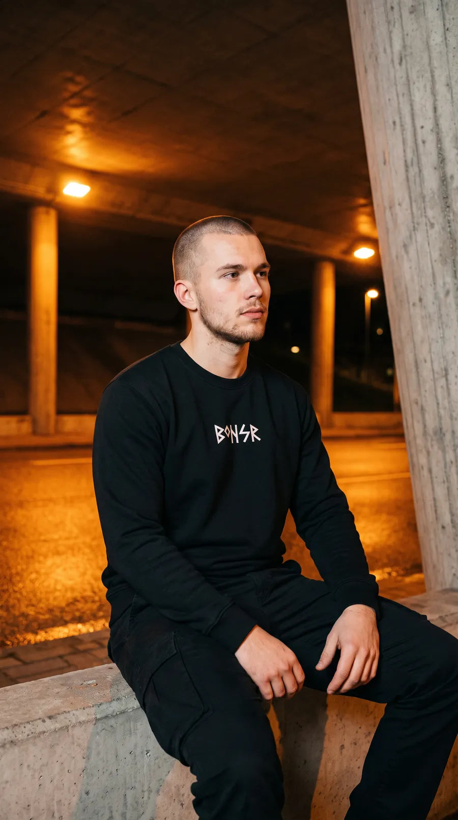 Mann im schwarzen Sweatshirt Nordic One sitzt auf einer Betonkante