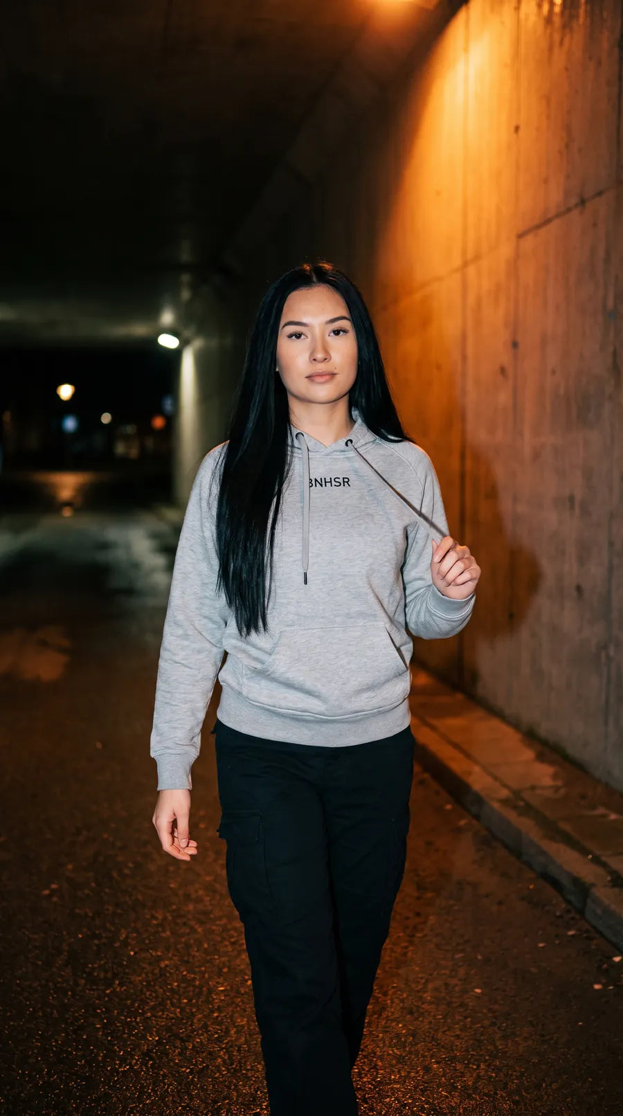 Frau im grauen BNHSR Hoodie in einer Unterführung bei Nacht