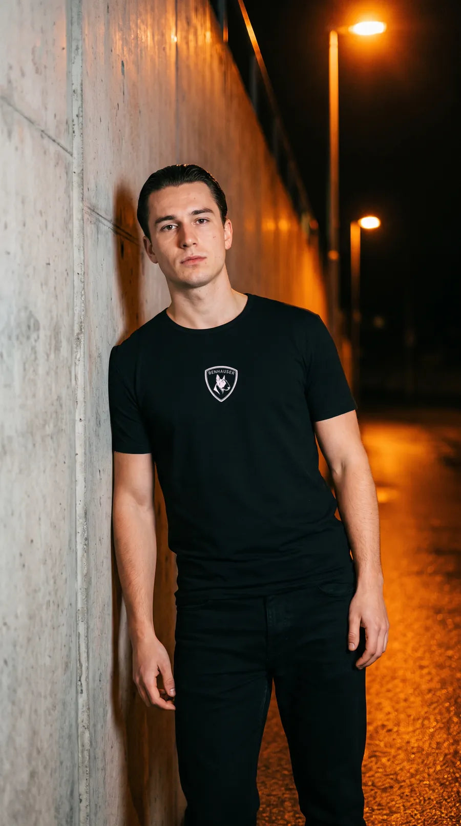 Mann im schwarzen Benhauser Classic T-Shirt an einer Betonwand