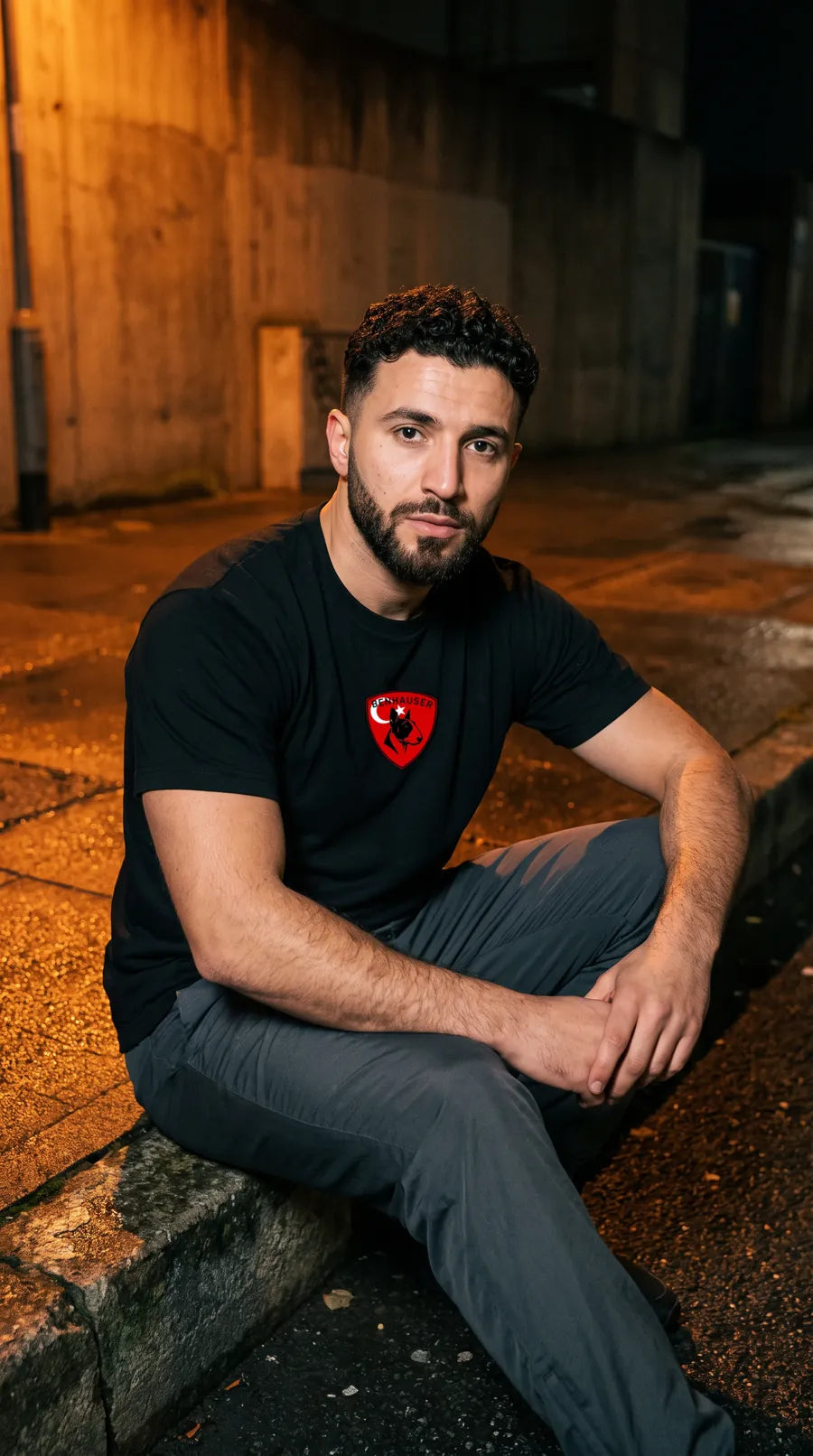Mann im schwarzen Türkei T-Shirt sitzt nachts auf einer Betonkante